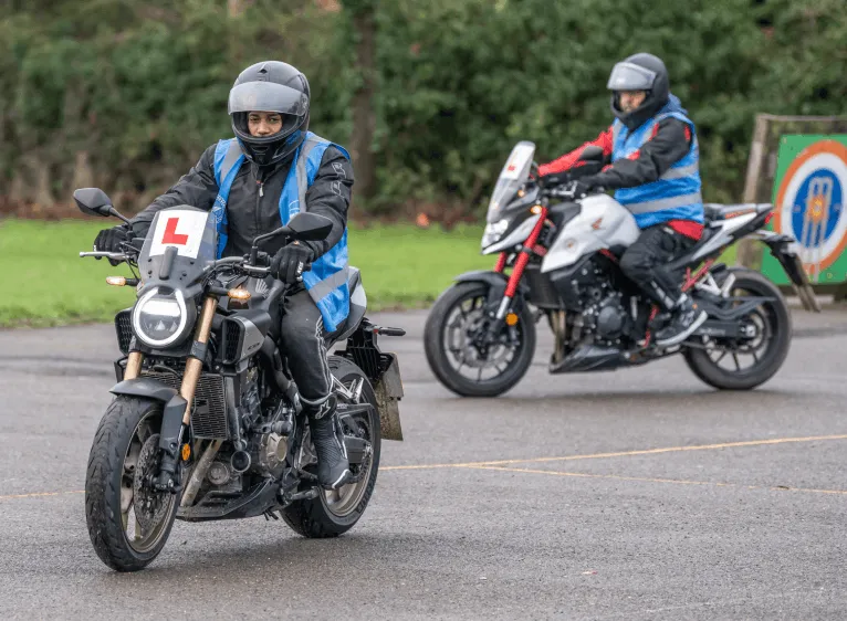 Two learner riders on training motorbikes at a Bikes in Motion session, the nearest wearing a blue student vest with an L plate.